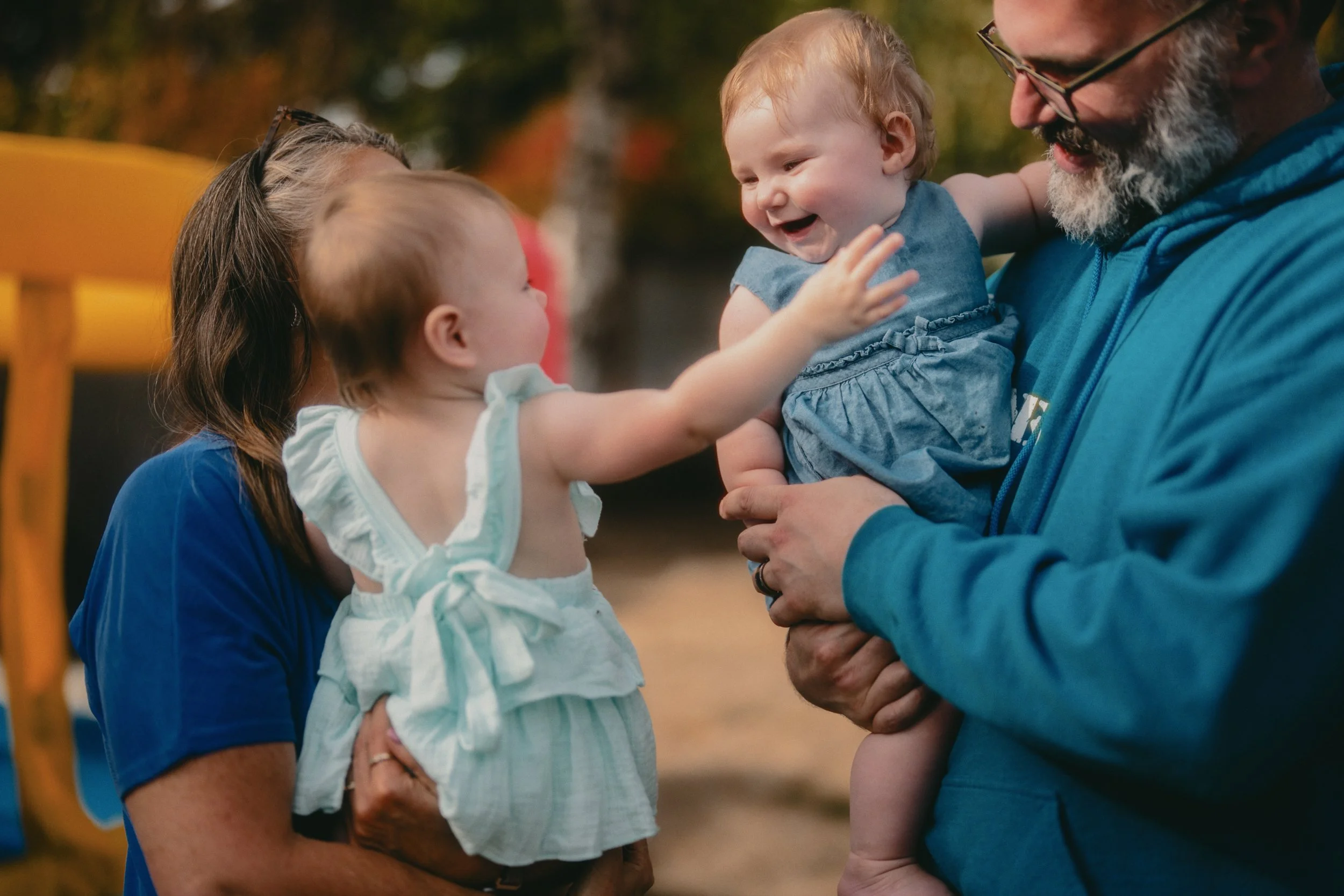 Parents smiling and holding a baby outdoors in warm sunset light.