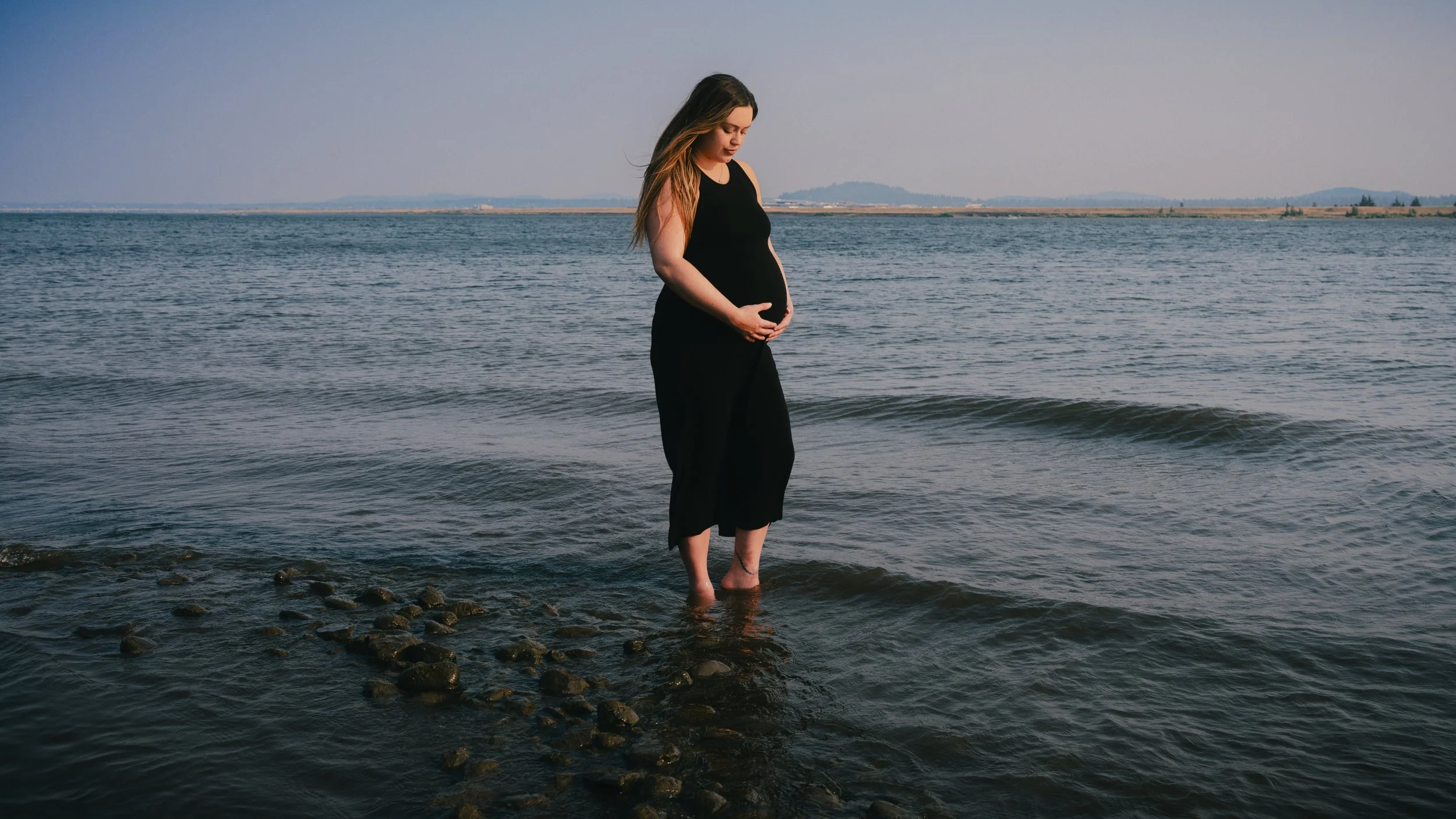 Pregnant woman standing in shallow water for a maternity portrait.