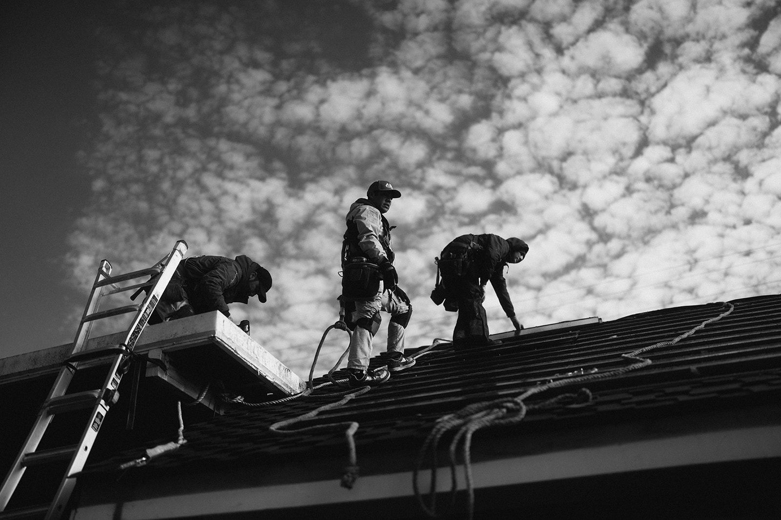Electricians working on a roof with ladders and tools in black and white.