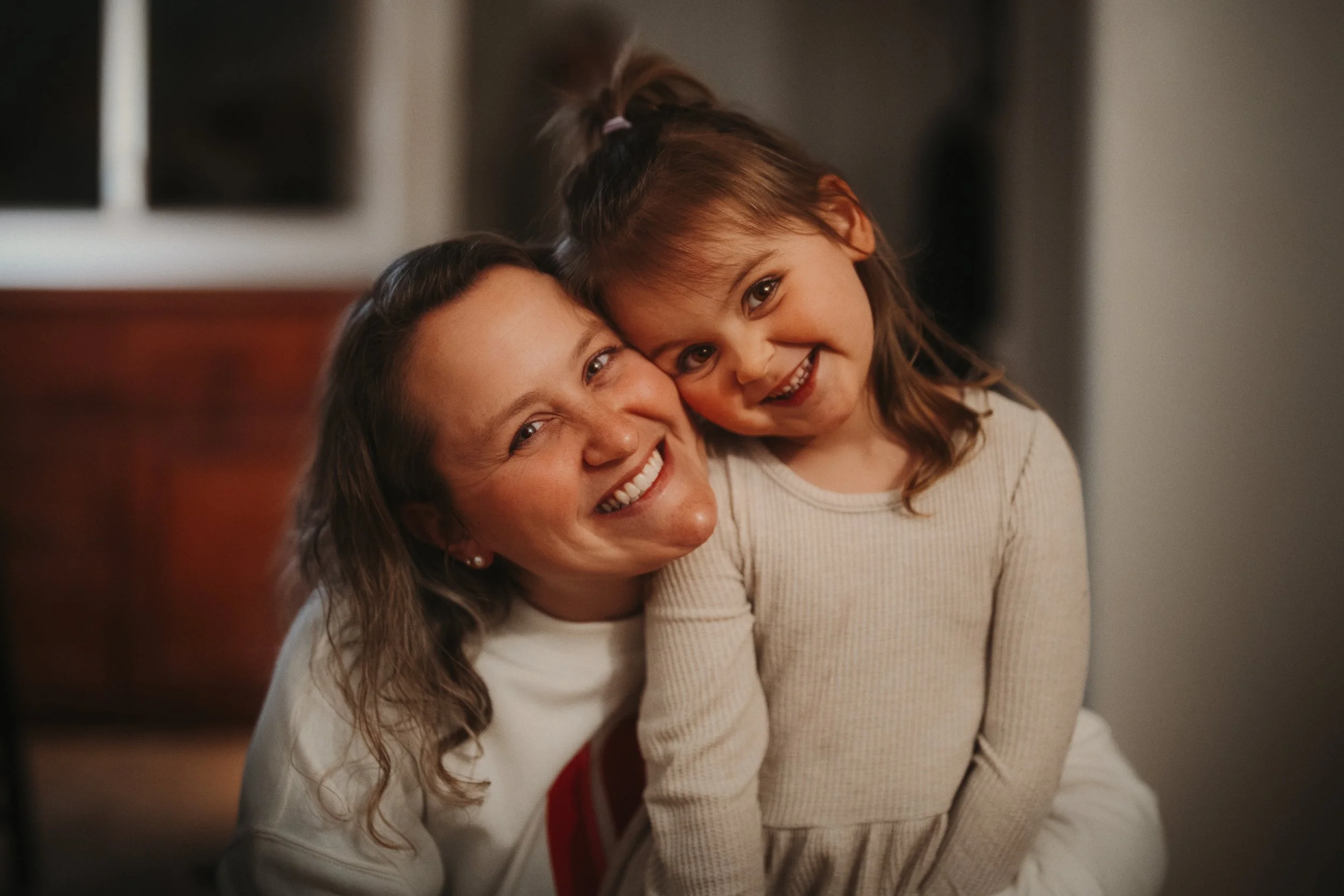 Mother and daughter smiling together in a warm indoor portrait.