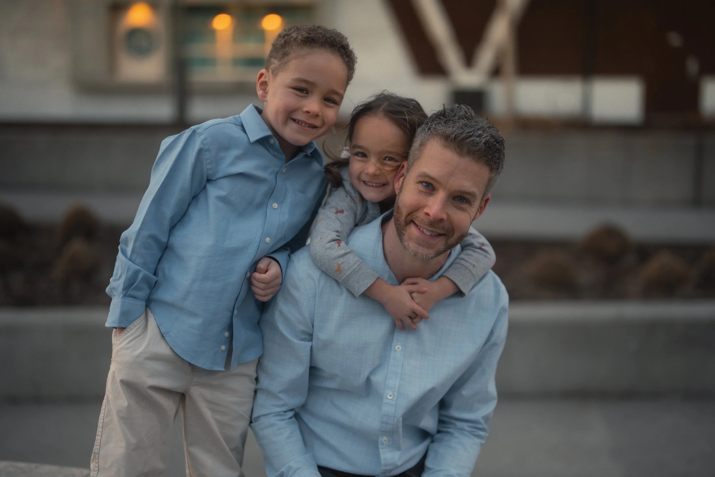 Family portrait of a father with two children smiling together outdoors.