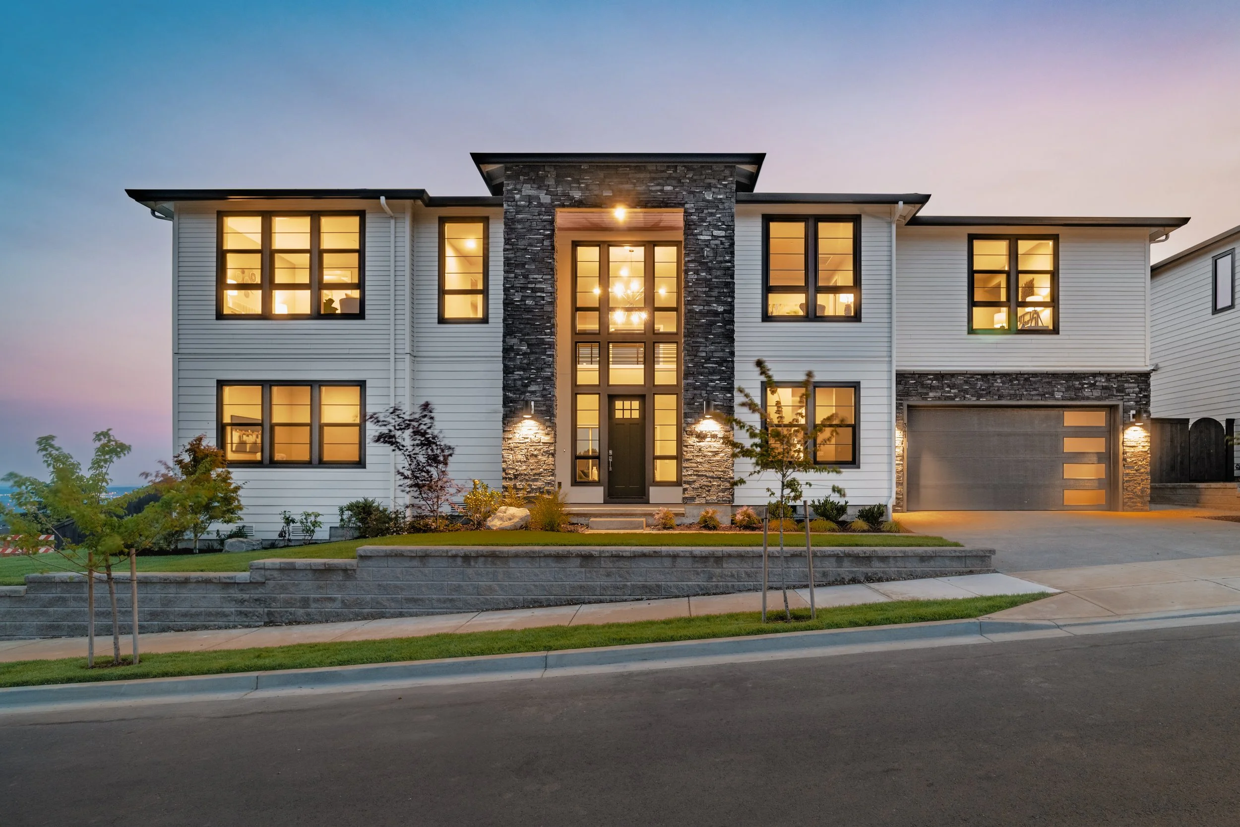 Modern two-story home exterior photographed at dusk with lights on.