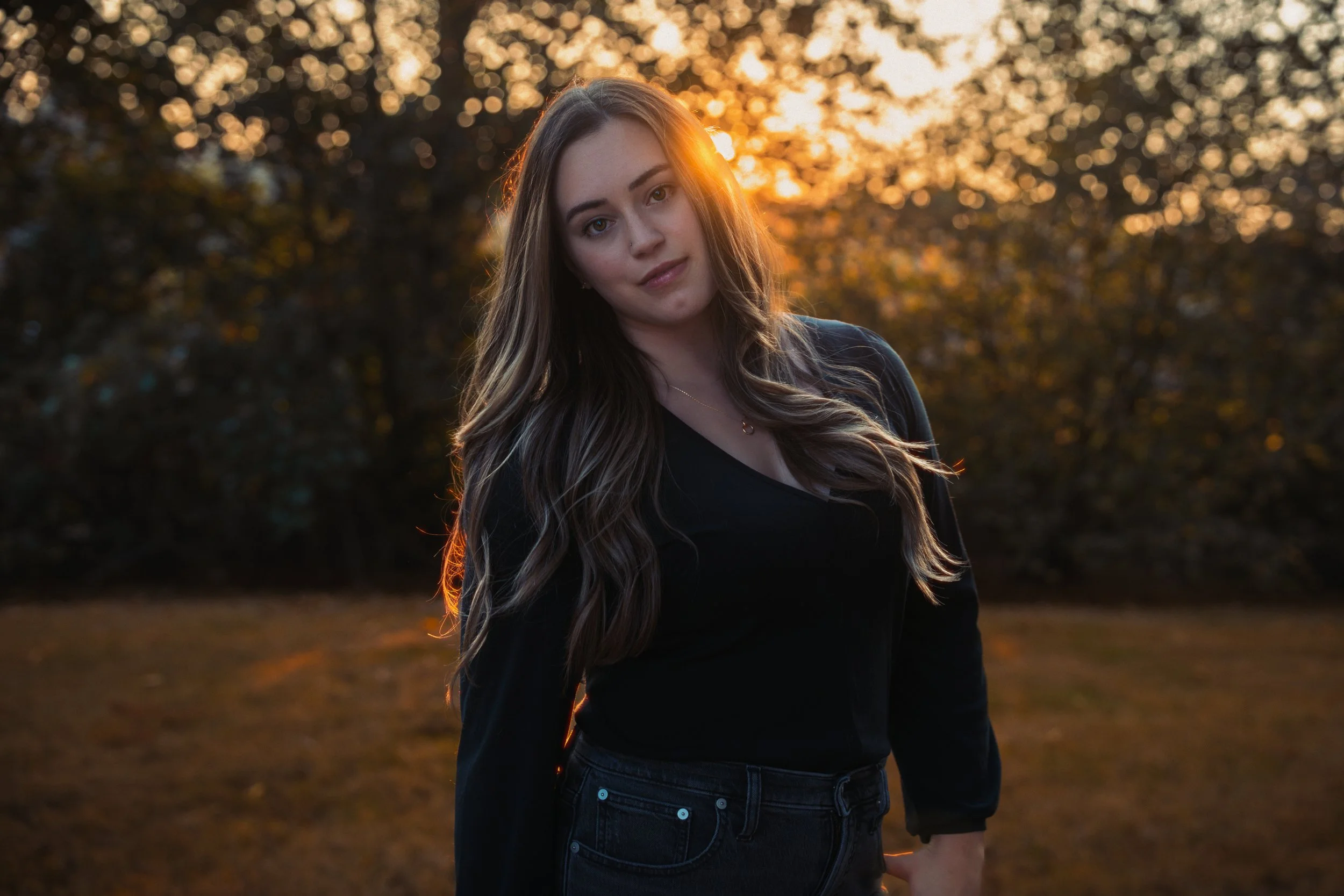 Portrait of a young woman standing outdoors in warm sunset light.